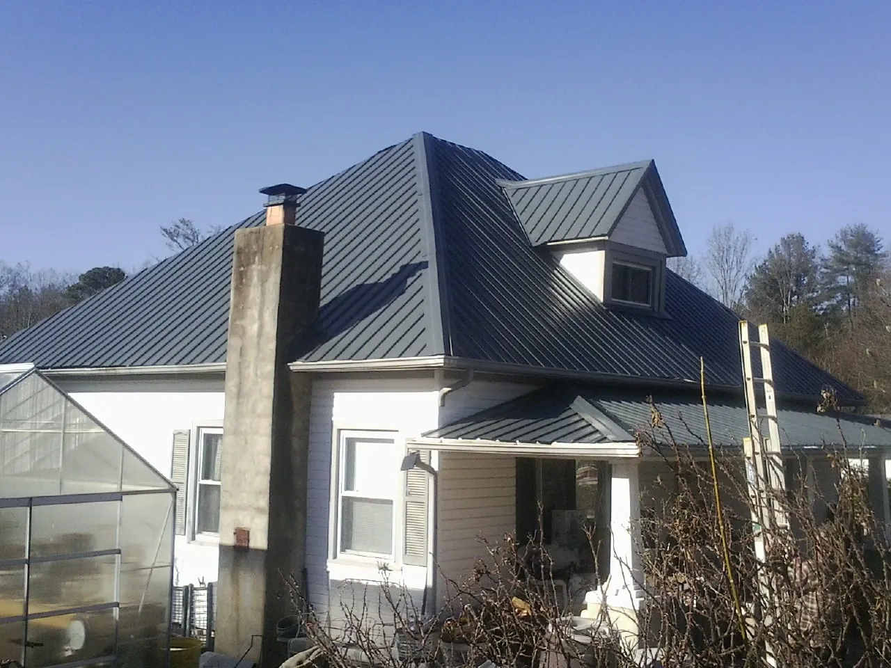 Dark blue standing seam metal roof on a white farmhouse with dormer — Slate & Tile Roof Repair by Roofing Brothers in Canandaigua