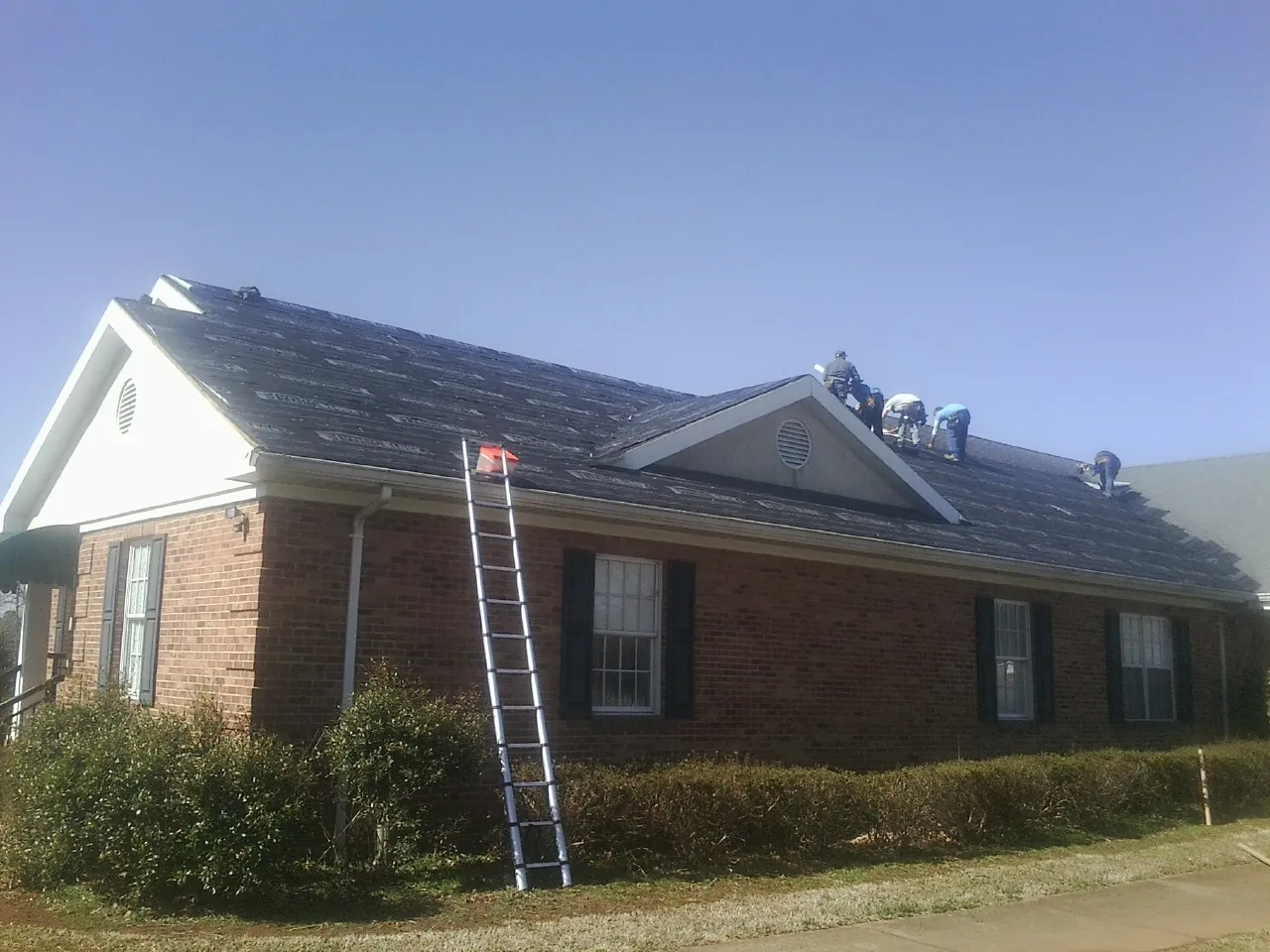 Crew tearing shingles off a brick ranch roof with a ladder set — Metal Roof Repair work by our crew in Canandaigua