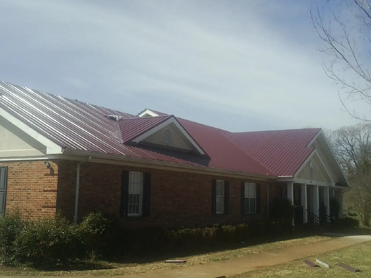 Red metal roof with gabled entries on a long brick building, from a Hail Damage Roof Repair job in Canandaigua