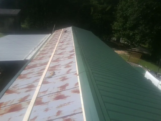 Old rusted panels beside newly installed green metal roofing — Wind Damage Roof Repair by Roofing Brothers in Canandaigua