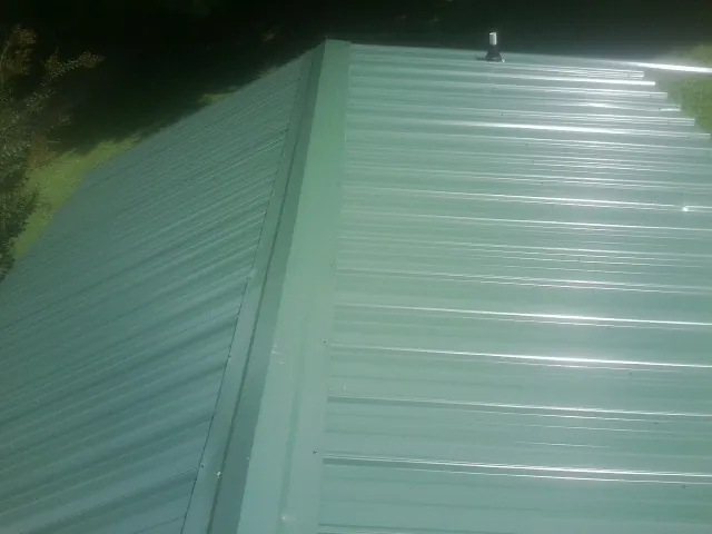New green metal panels meeting at the ridge of a roof — Flat Roof Repair work by our crew in Canandaigua