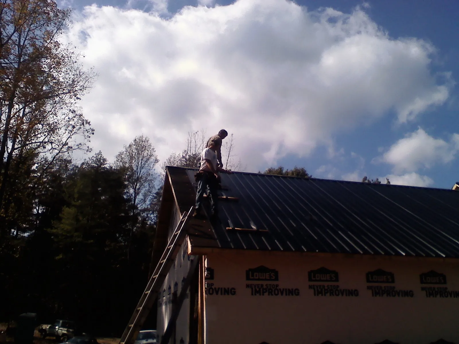 Roofer fastening dark metal panels high against a cloudy sky, from a Roof Inspection job in Canandaigua