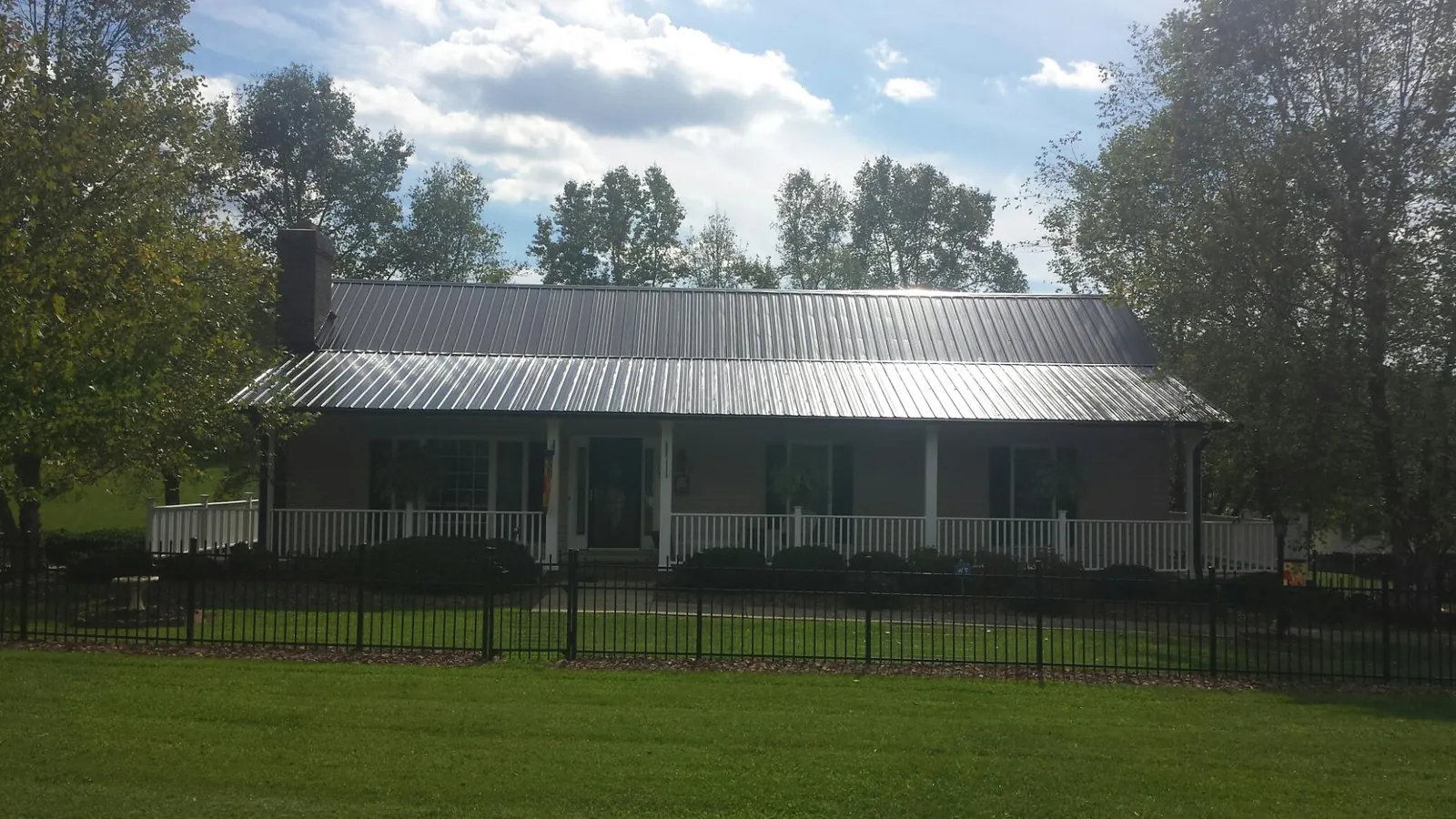 Gray metal roof on a brick ranch with a full width front porch — Gutter Guard Installation work by our crew in Canandaigua