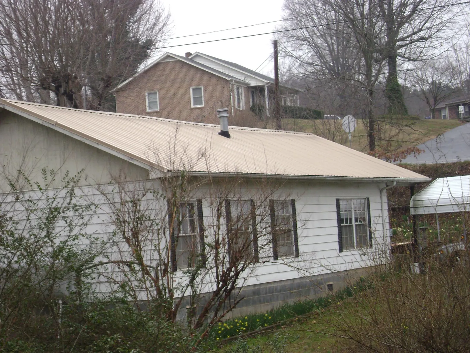 Tan metal roof on a white sided house set into a hillside — Commercial Roofing by Roofing Brothers in Canandaigua
