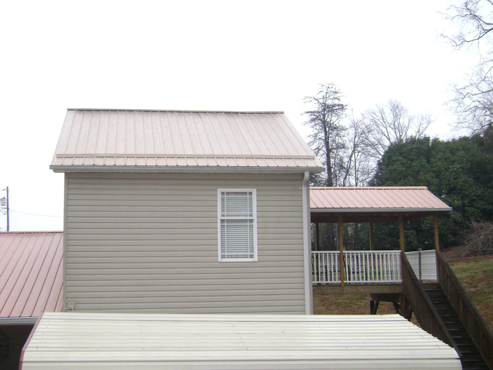 Tan metal roofs on a two story addition and attached porch, from a Roof Replacement job in Canandaigua